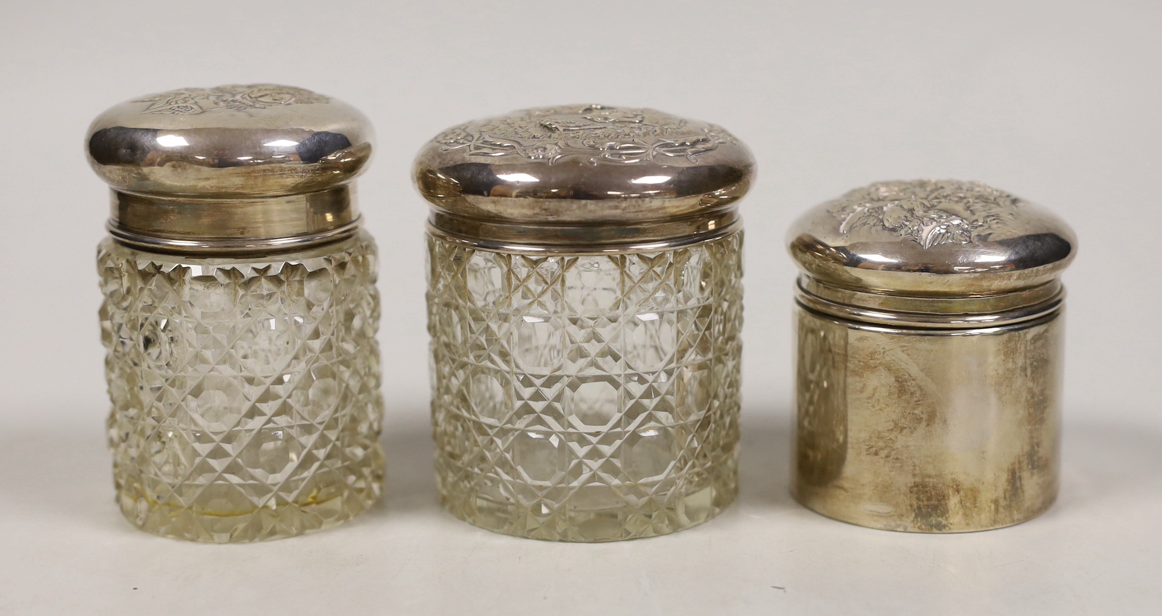 Two early 20th century silver mounted glass Reynolds angel lid toilet jars, tallest 89mm and one other silver mounted toilet jar.